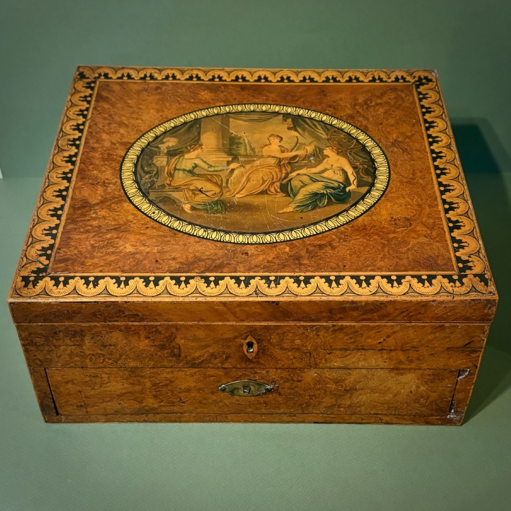 A square Regency burr walnut workbox with a central classical medallion print, decorative printed border, brass side handles, and a lower drawer. View IV