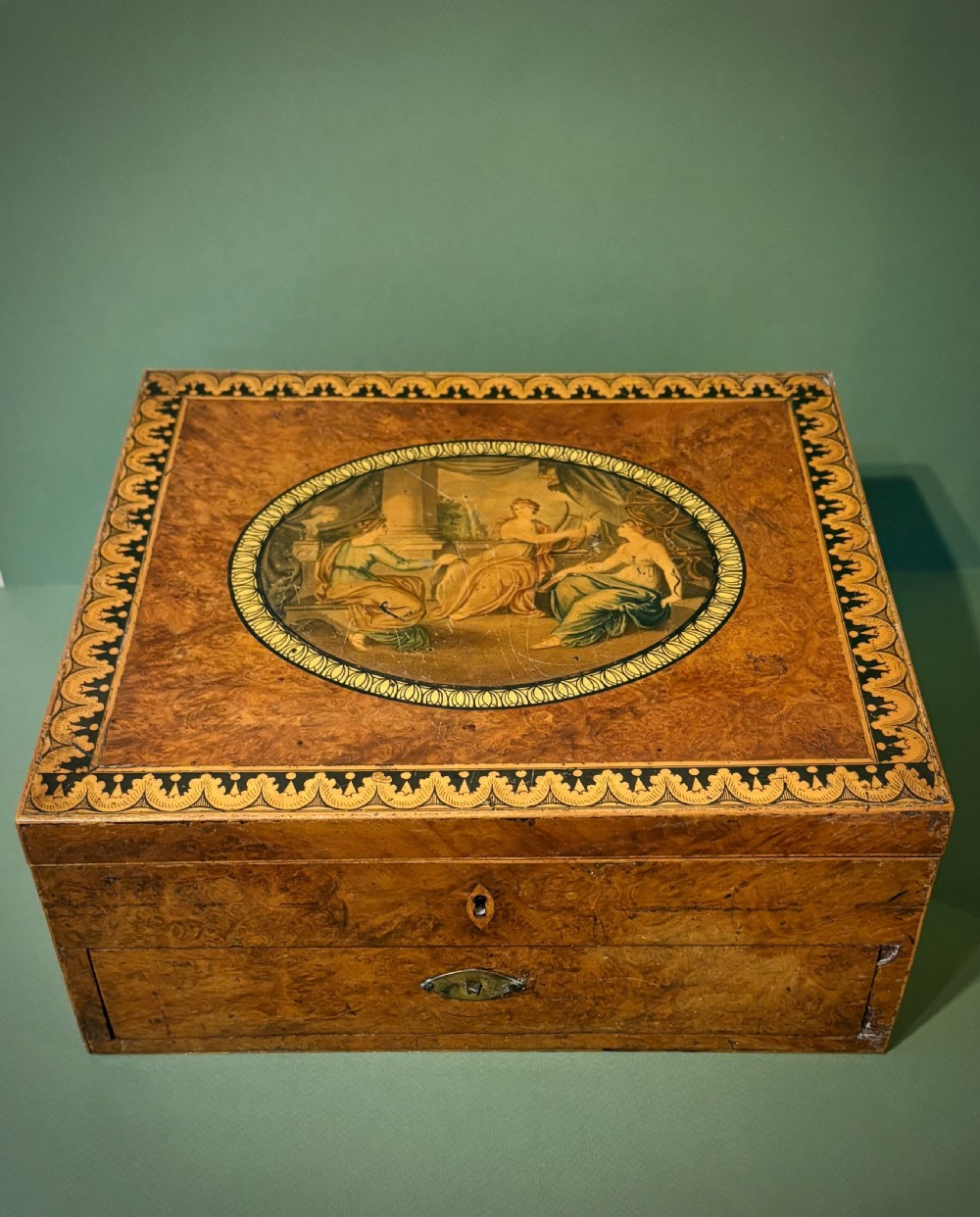A square Regency burr walnut workbox with a central classical medallion print, decorative printed border, brass side handles, and a lower drawer. View VII