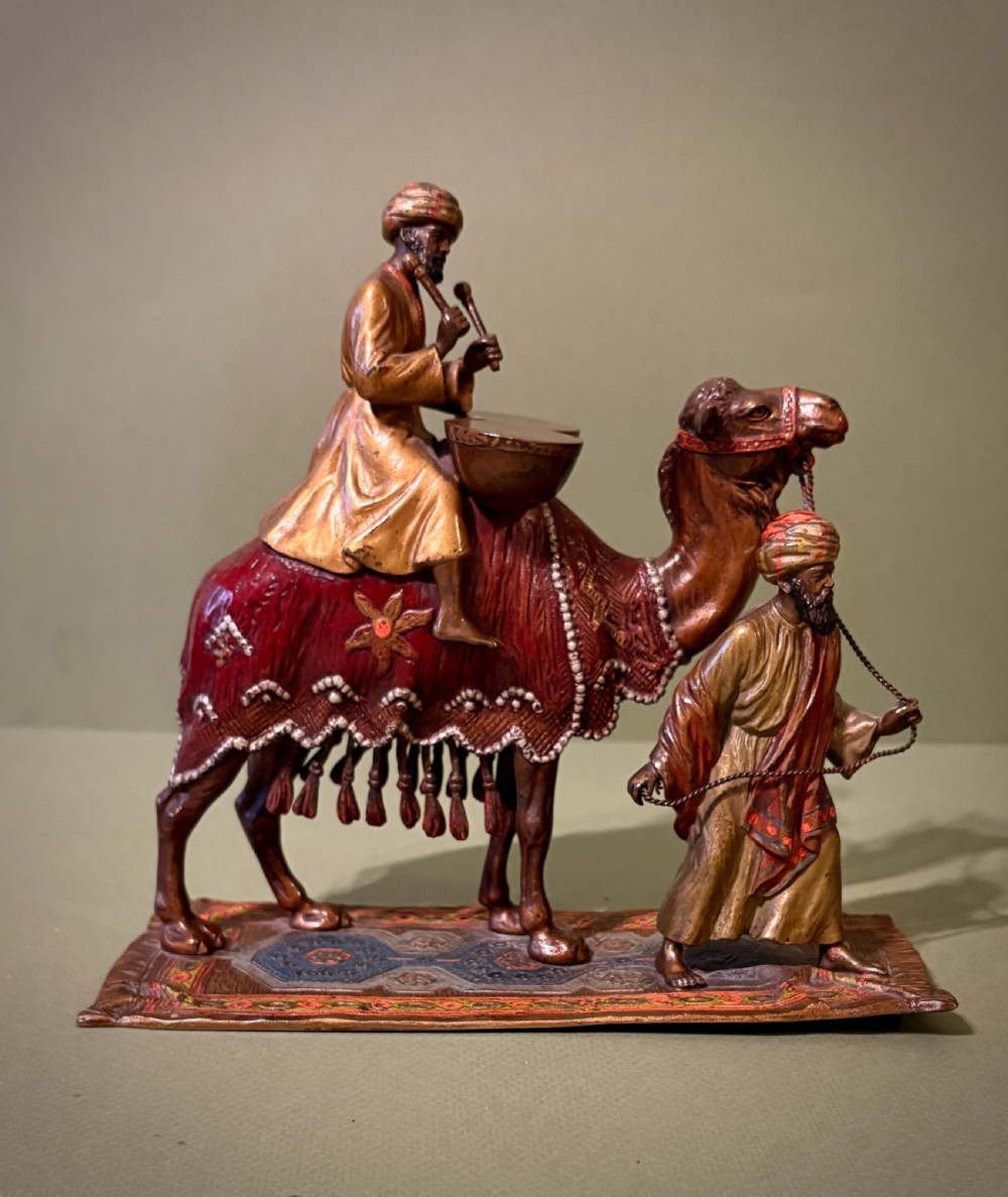 A cold-painted Vienna bronze group depicting a camel musician playing drums led by a standing figure on a cast bronze carpet base.