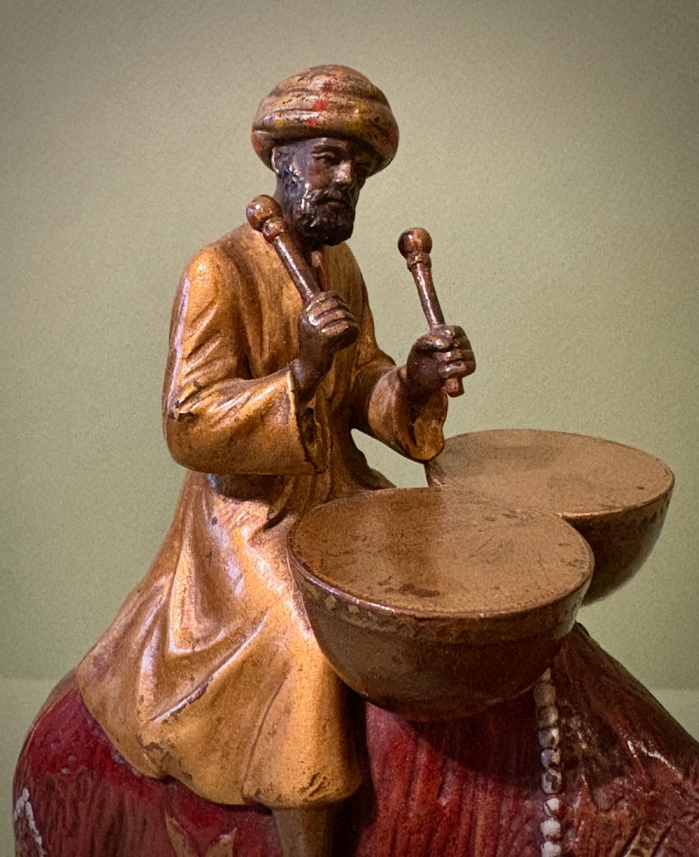 A cold-painted Vienna bronze group depicting a camel musician playing drums led by a standing figure on a cast bronze carpet base. View II