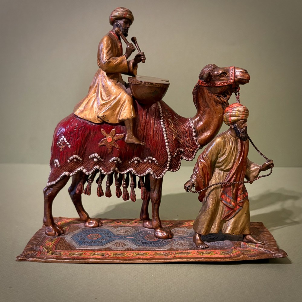A cold-painted Vienna bronze group depicting a camel musician playing drums led by a standing figure on a cast bronze carpet base. View V