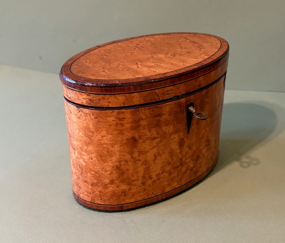 An oval George III satinwood tea caddy featuring inlaid crossbanding, a dark keyhole escutcheon, and an accompanying metal key. View II