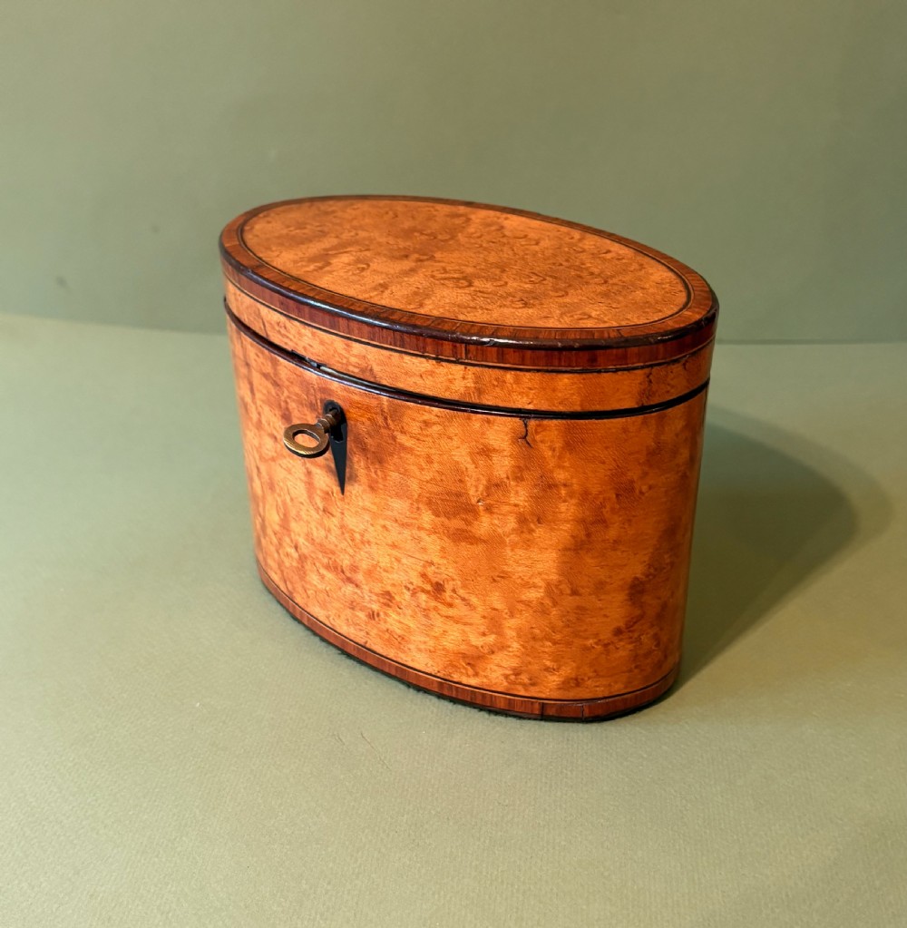 An oval George III satinwood tea caddy featuring inlaid crossbanding, a dark keyhole escutcheon, and an accompanying metal key. View III