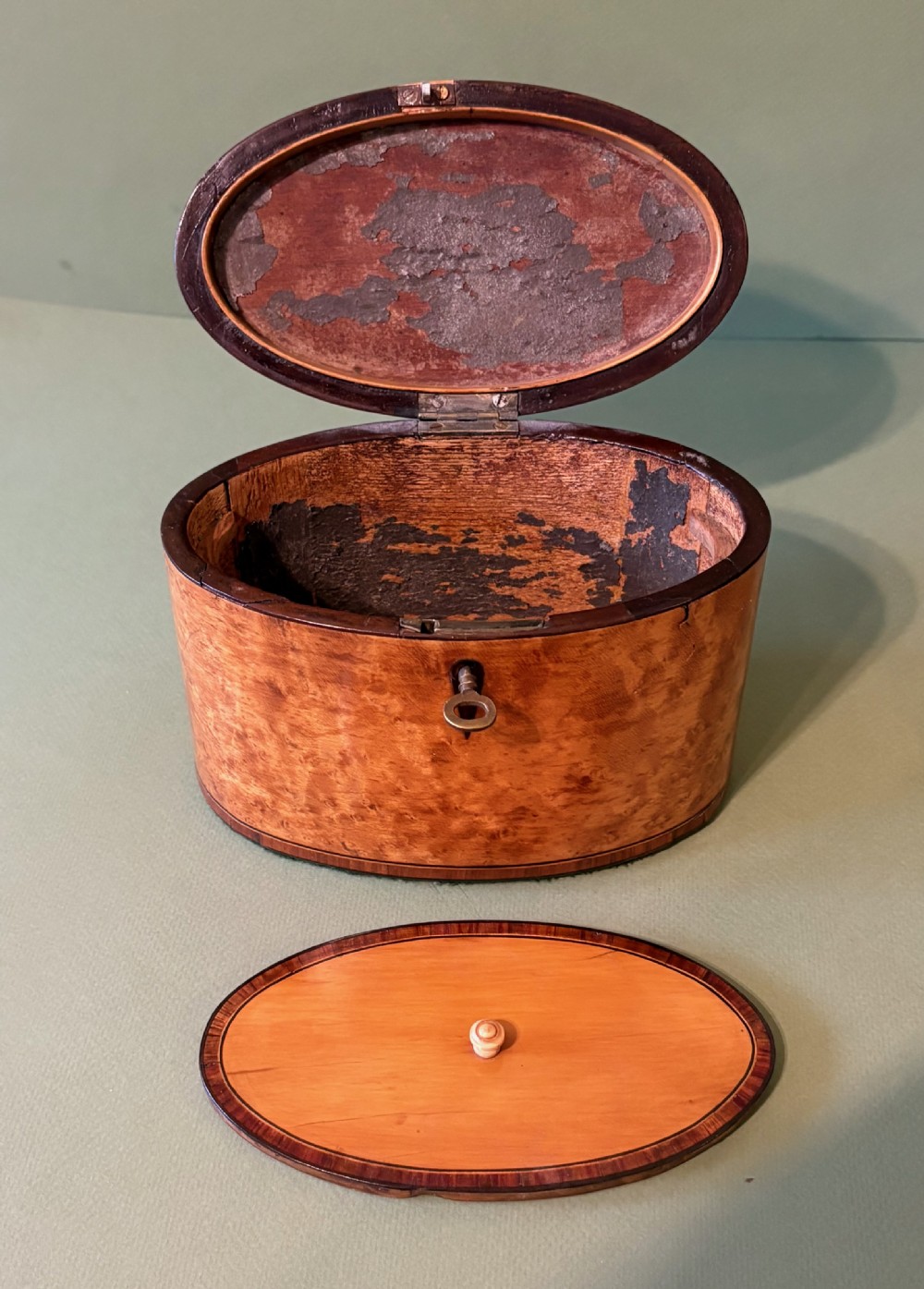 An oval George III satinwood tea caddy featuring inlaid crossbanding, a dark keyhole escutcheon, and an accompanying metal key. View V