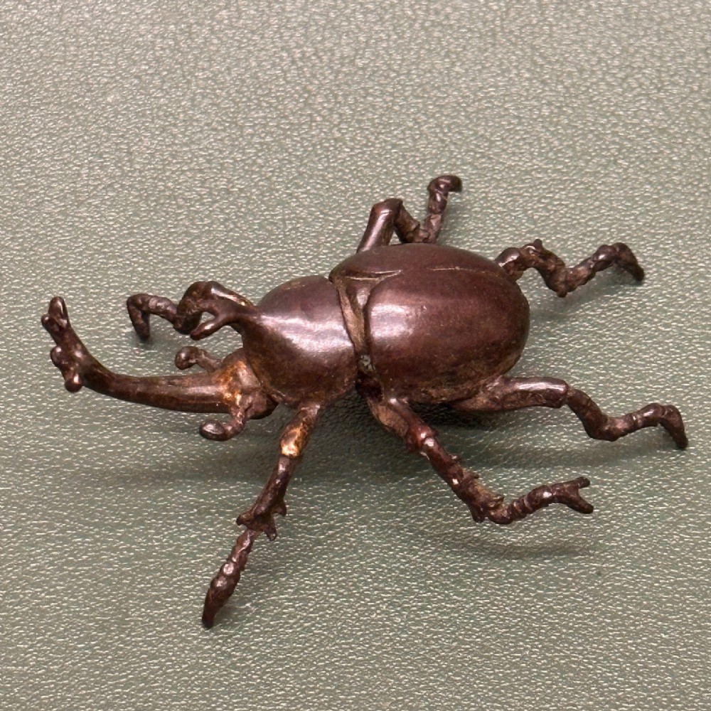 A Japanese Meiji period cast bronze sculpture of a rhinoceros beetle with textured legs and a dark brown patina.