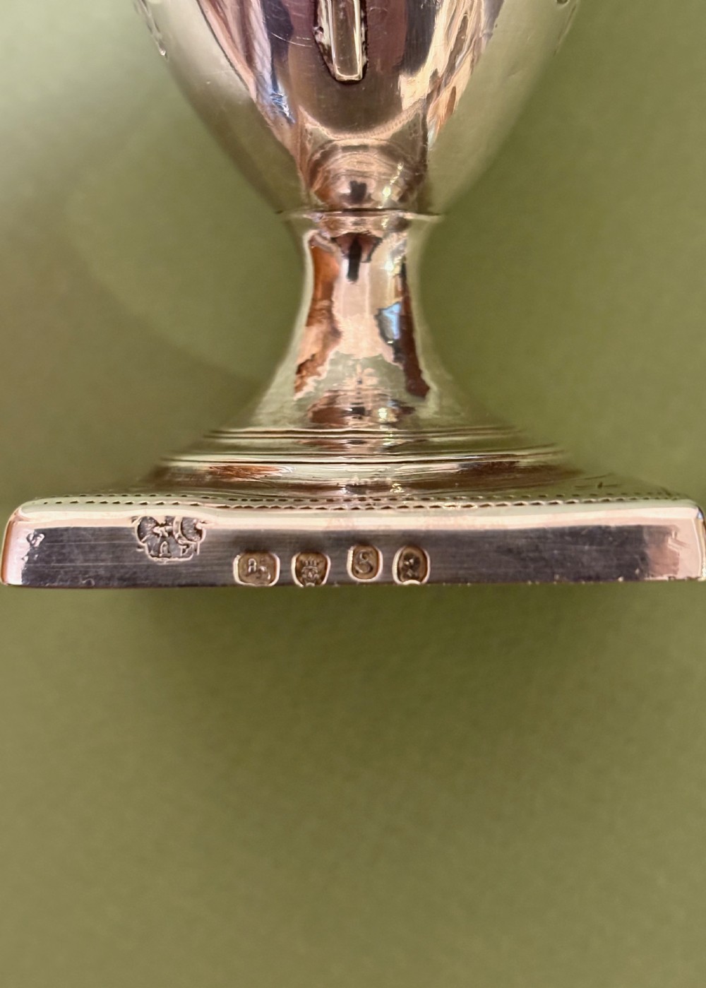 A George III sterling silver helmet-shaped cream jug featuring bright-cut floral engraving, a high loop handle, and a square pedestal base. View IV