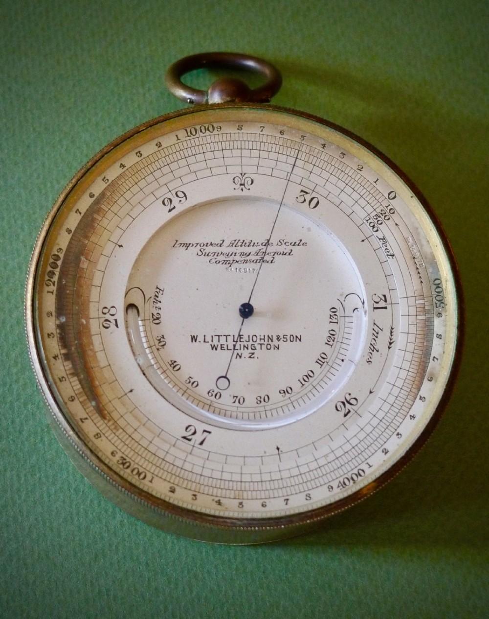 A circular brass pocket aneroid barometer featuring a silvered dial with dual altitude markings and a suspension ring at the top. View II