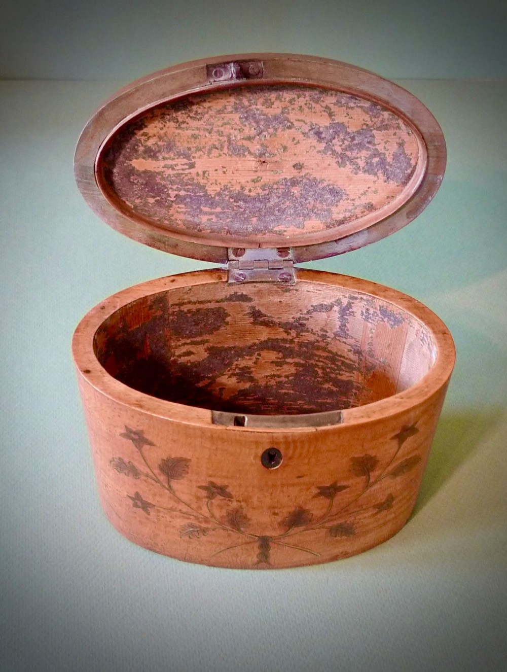An oval Georgian satinwood tea caddy featuring floral wood inlay on the front, a top brass handle, and a central keyhole escutcheon. View III