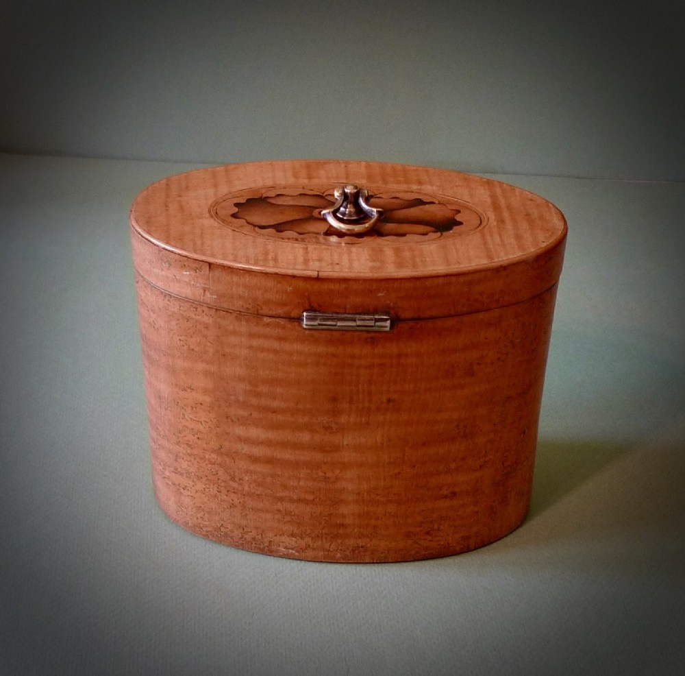 An oval Georgian satinwood tea caddy featuring floral wood inlay on the front, a top brass handle, and a central keyhole escutcheon. View IV