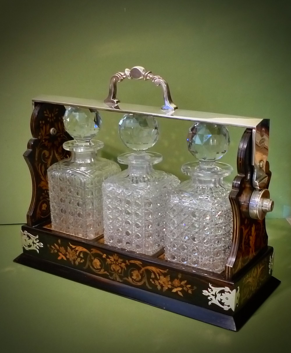 A Victorian three-bottle cut crystal decanter tantalus housed in a dark wooden frame with floral marquetry inlay and a silver-toned metal locking top handle. View II