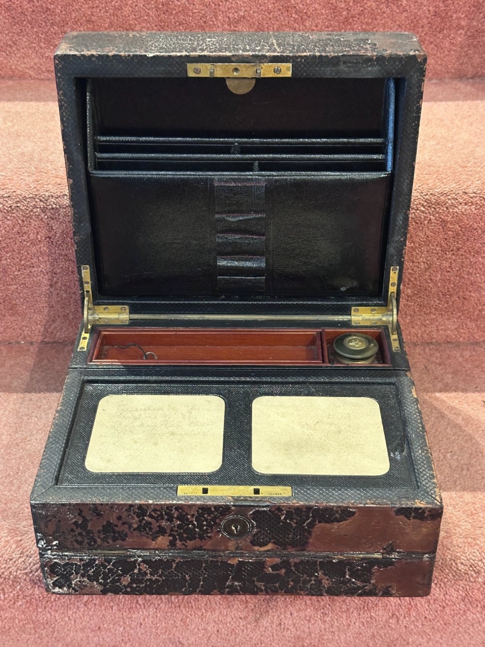 An open Victorian leather-bound writing box featuring internal letter slots, a pen tray, an inkwell compartment, and brass hardware.
