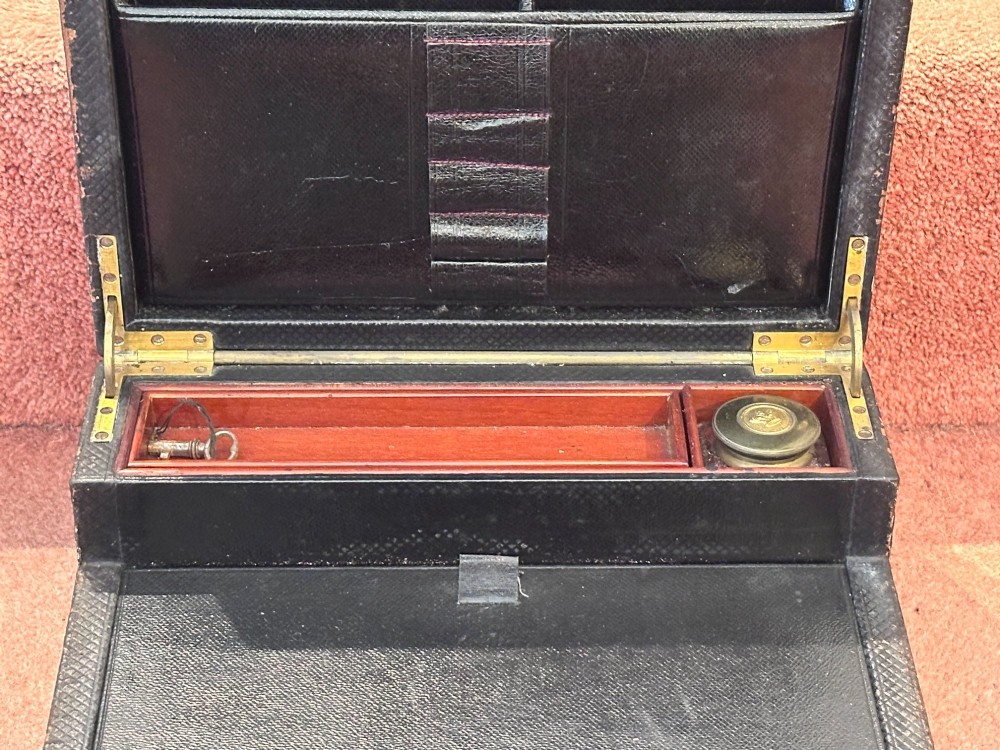 An open Victorian leather-bound writing box featuring internal letter slots, a pen tray, an inkwell compartment, and brass hardware. View IV