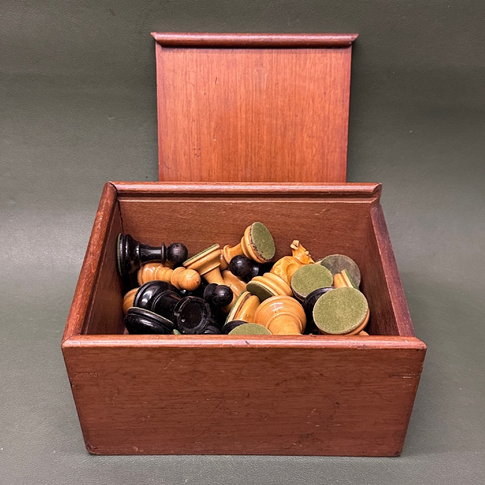A complete set of carved boxwood and ebonised black Staunton pattern chess pieces displayed in front of a warm mahogany wooden box with a sliding lid. View II