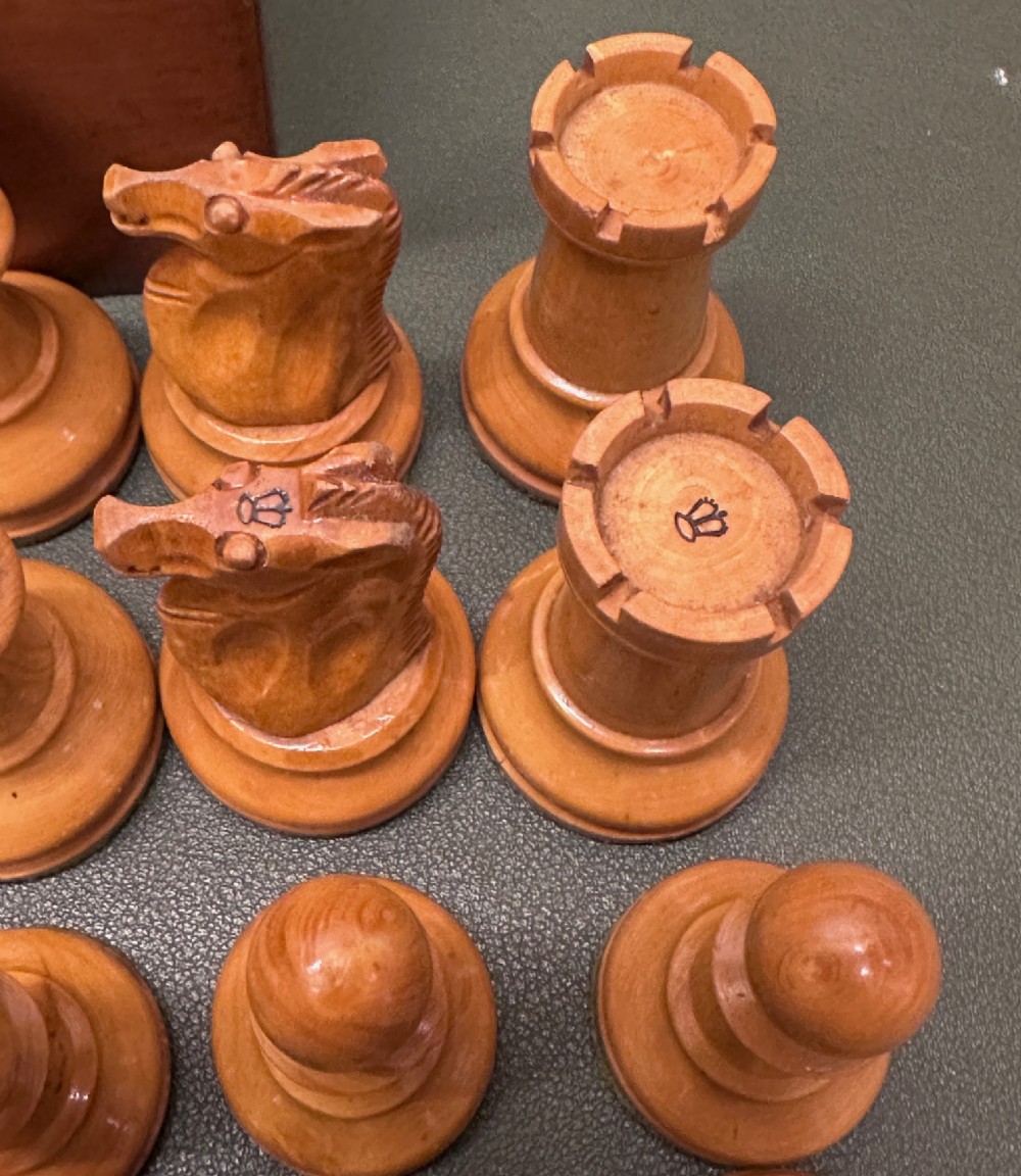 A complete set of carved boxwood and ebonised black Staunton pattern chess pieces displayed in front of a warm mahogany wooden box with a sliding lid. View VII
