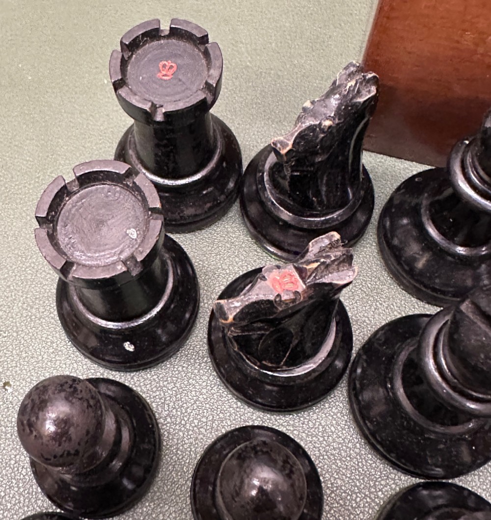 A complete set of carved boxwood and ebonised black Staunton pattern chess pieces displayed in front of a warm mahogany wooden box with a sliding lid. View VIII