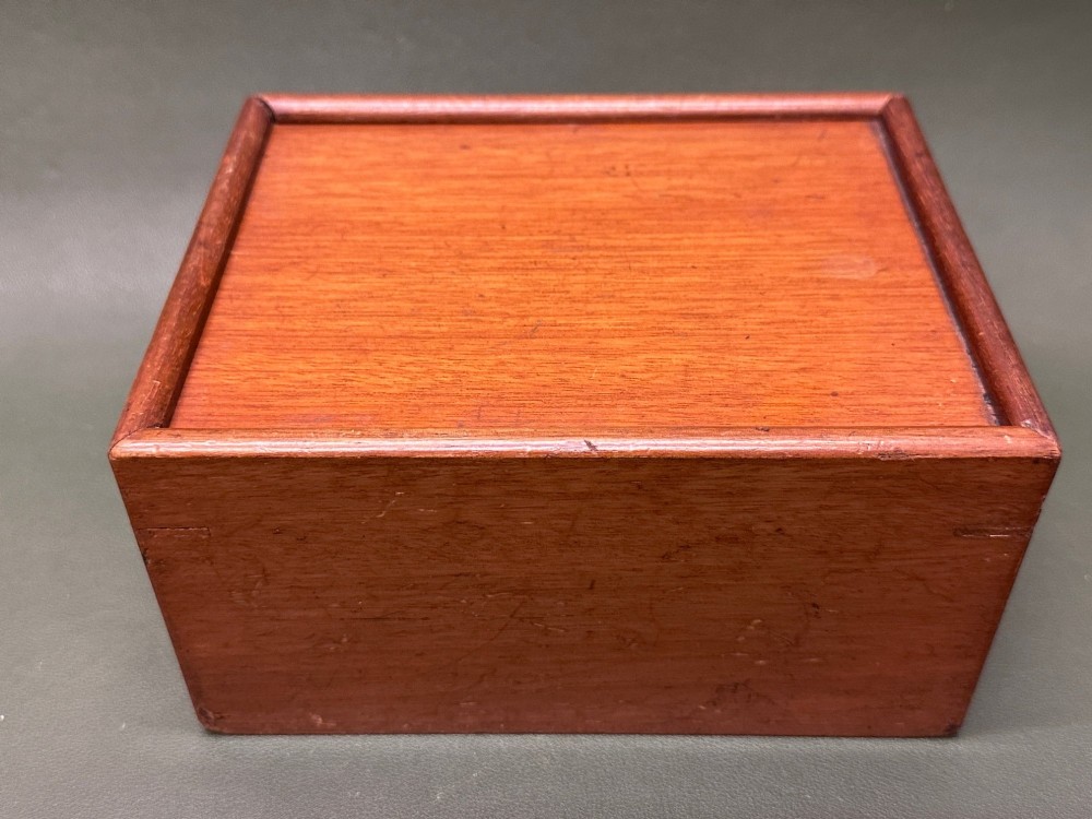 A complete set of carved boxwood and ebonised black Staunton pattern chess pieces displayed in front of a warm mahogany wooden box with a sliding lid. View IX