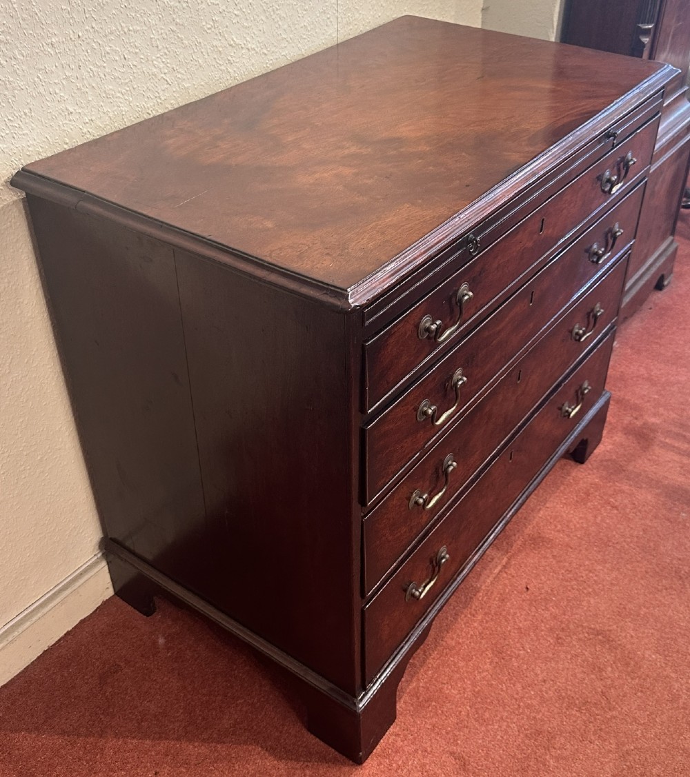 A George III dark mahogany bachelors chest featuring four graduated drawers, brass swan-neck handles, keyhole escutcheons, a pull-out brushing slide, and bracket feet. View II