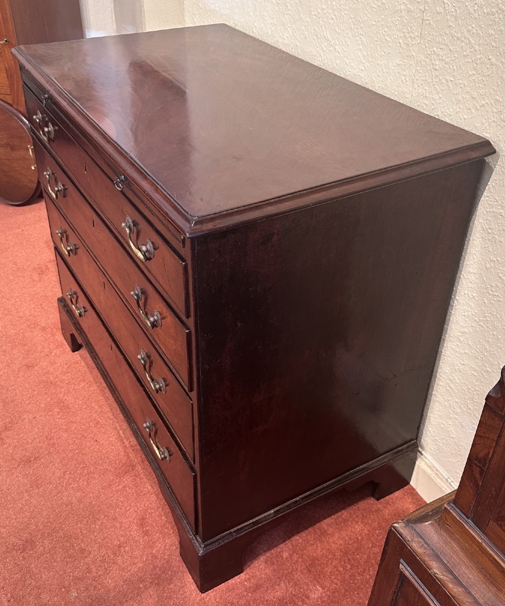 A George III dark mahogany bachelors chest featuring four graduated drawers, brass swan-neck handles, keyhole escutcheons, a pull-out brushing slide, and bracket feet. View III