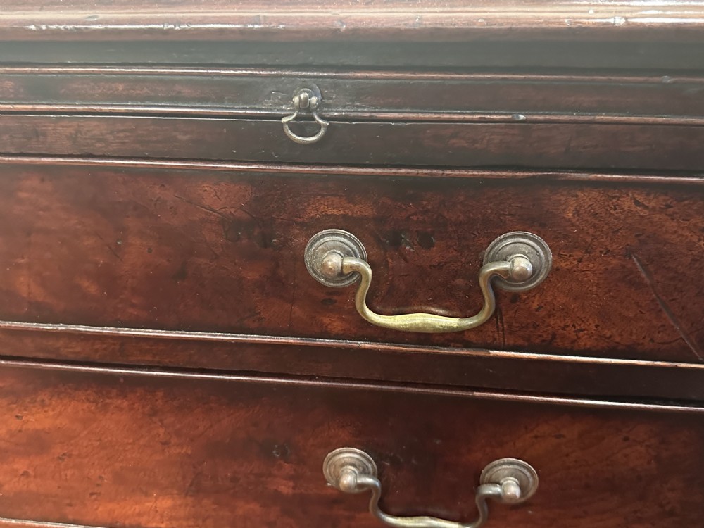 A George III dark mahogany bachelors chest featuring four graduated drawers, brass swan-neck handles, keyhole escutcheons, a pull-out brushing slide, and bracket feet. View IV