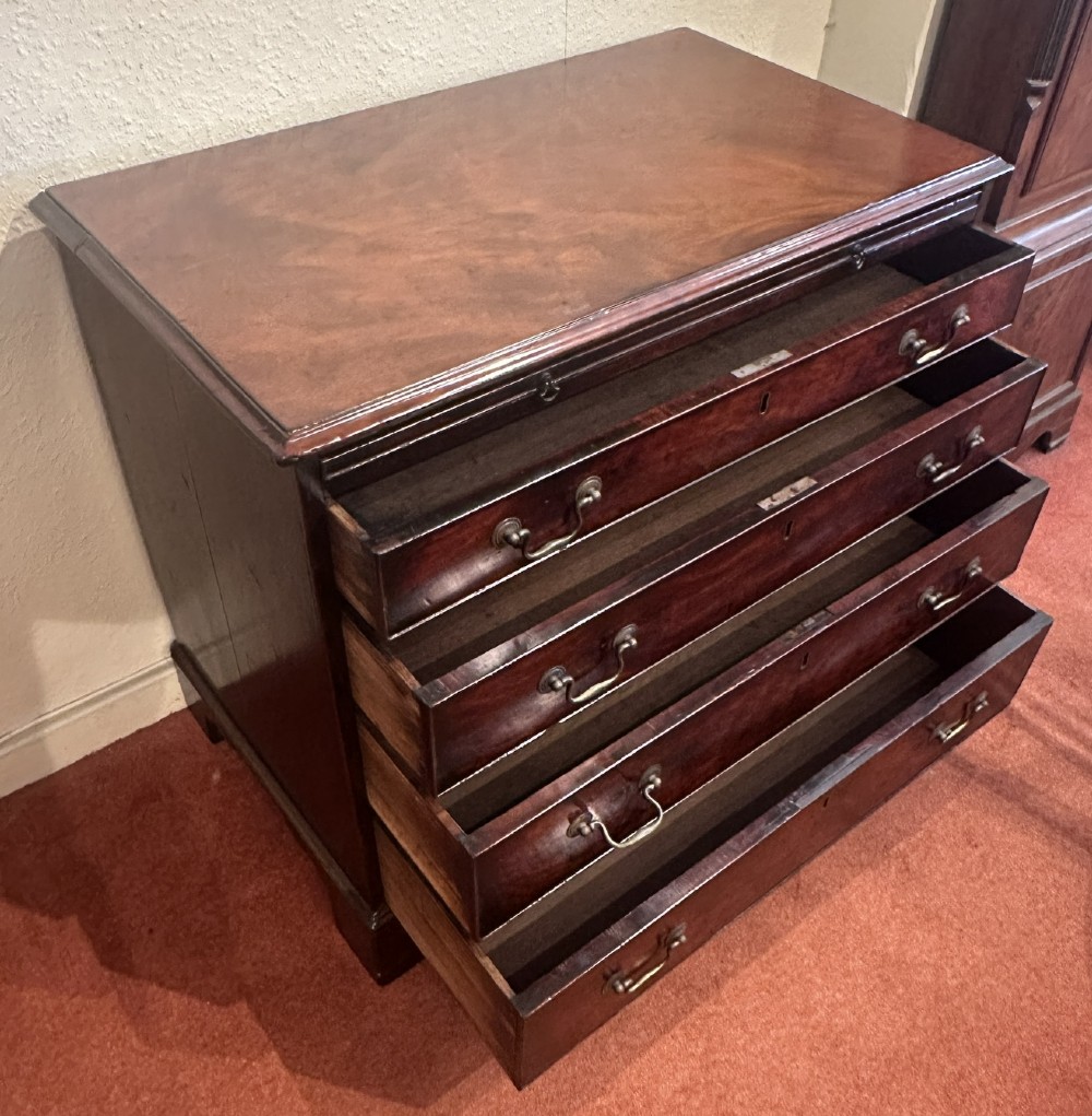 A George III dark mahogany bachelors chest featuring four graduated drawers, brass swan-neck handles, keyhole escutcheons, a pull-out brushing slide, and bracket feet. View VI
