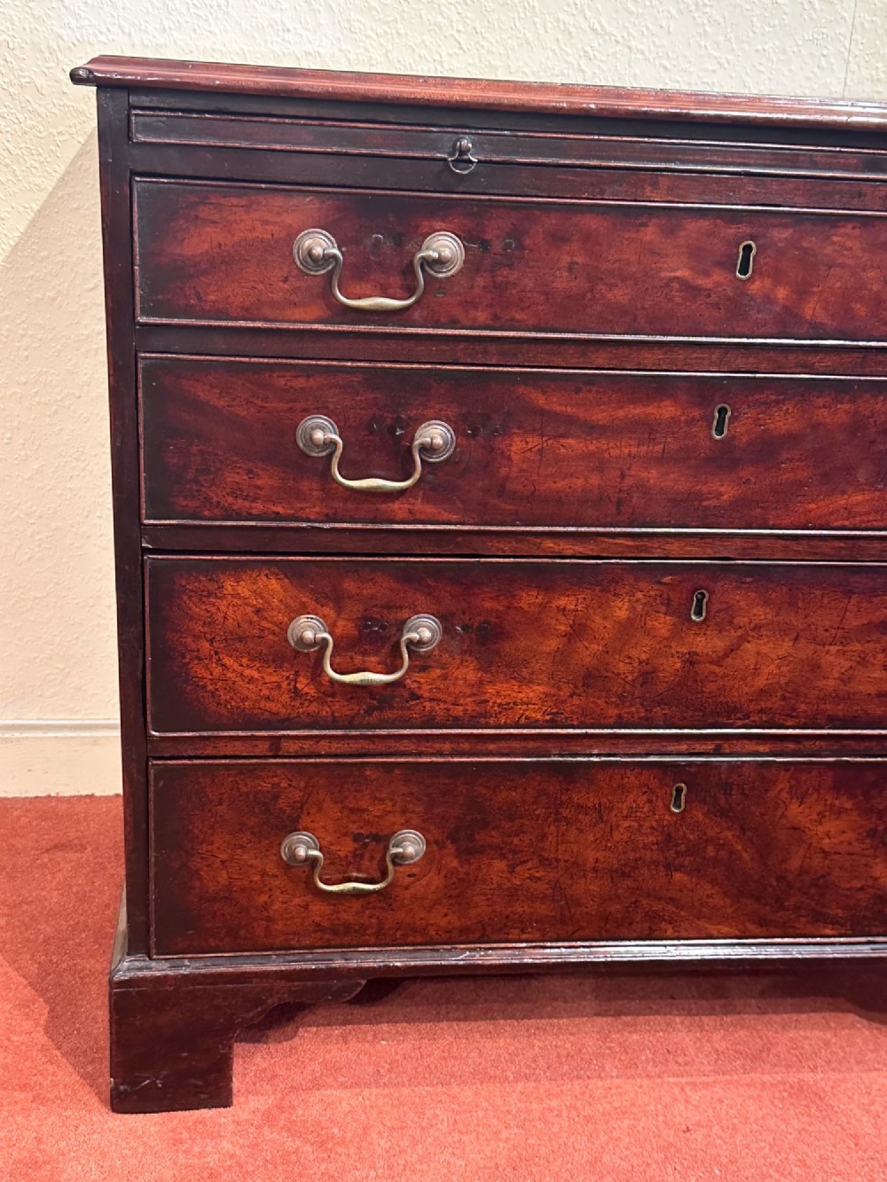 A George III dark mahogany bachelors chest featuring four graduated drawers, brass swan-neck handles, keyhole escutcheons, a pull-out brushing slide, and bracket feet. View VIII