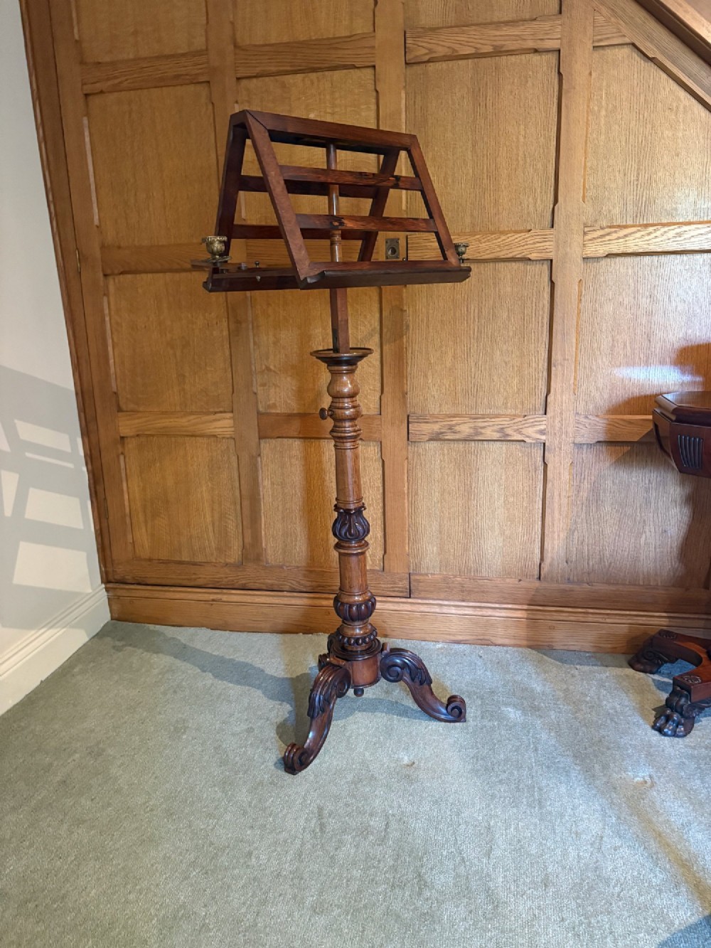 An antique mahogany duet music stand with a double slatted desk, brass candle sconces, a turned central column, and carved tripod scroll legs. View IV