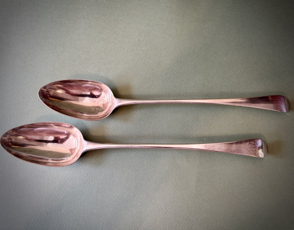 A pair of 18th-century sterling silver basting spoons featuring elongated handles with engraved monograms and oval bowls.