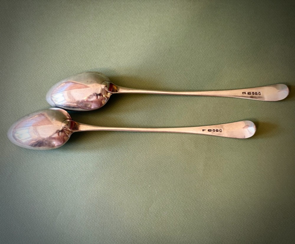 A pair of 18th-century sterling silver basting spoons featuring elongated handles with engraved monograms and oval bowls. View II