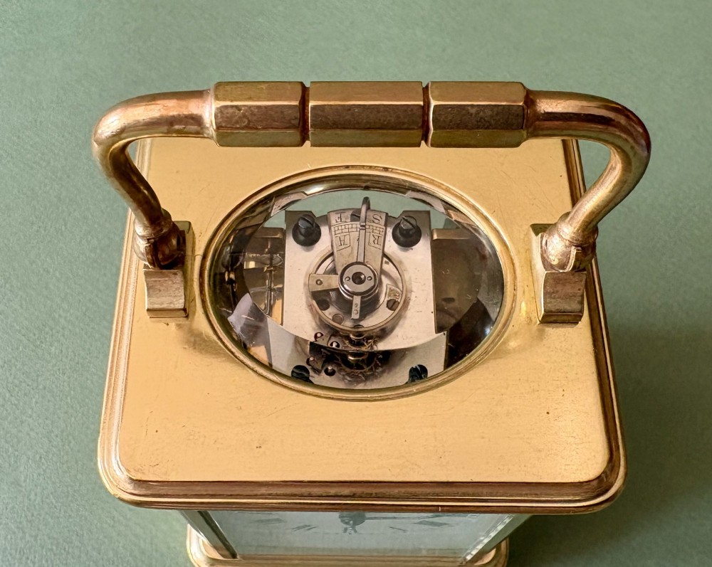 A nineteenth-century French carriage clock featuring a gilt brass case, glass side panels, a hinged top handle, and a white enamel dial with black Roman numerals. View III