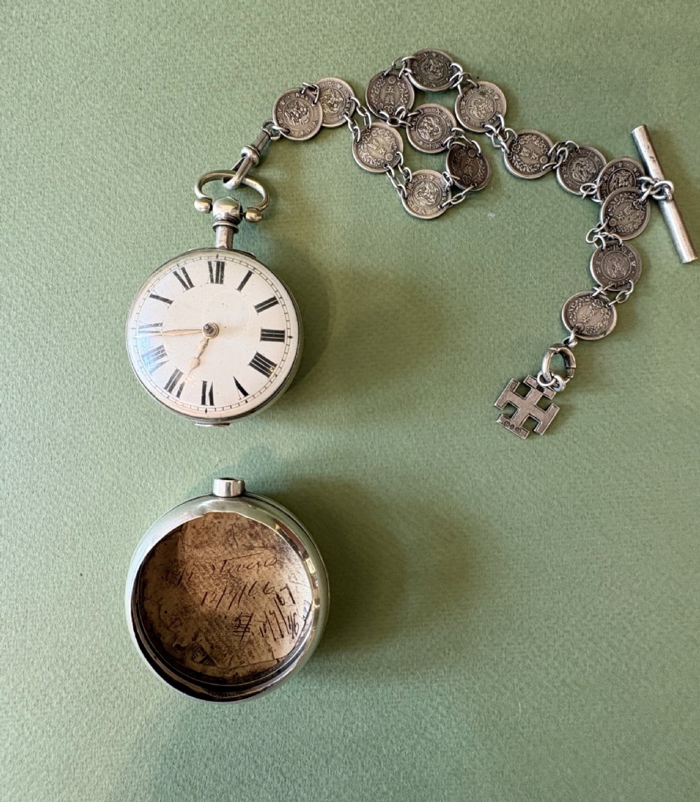 An antique silver pair-cased pocket watch featuring a white enamel dial with black Roman numerals, connected to a silver chain formed of linked coins, a T-bar, and a small cross charm. View II