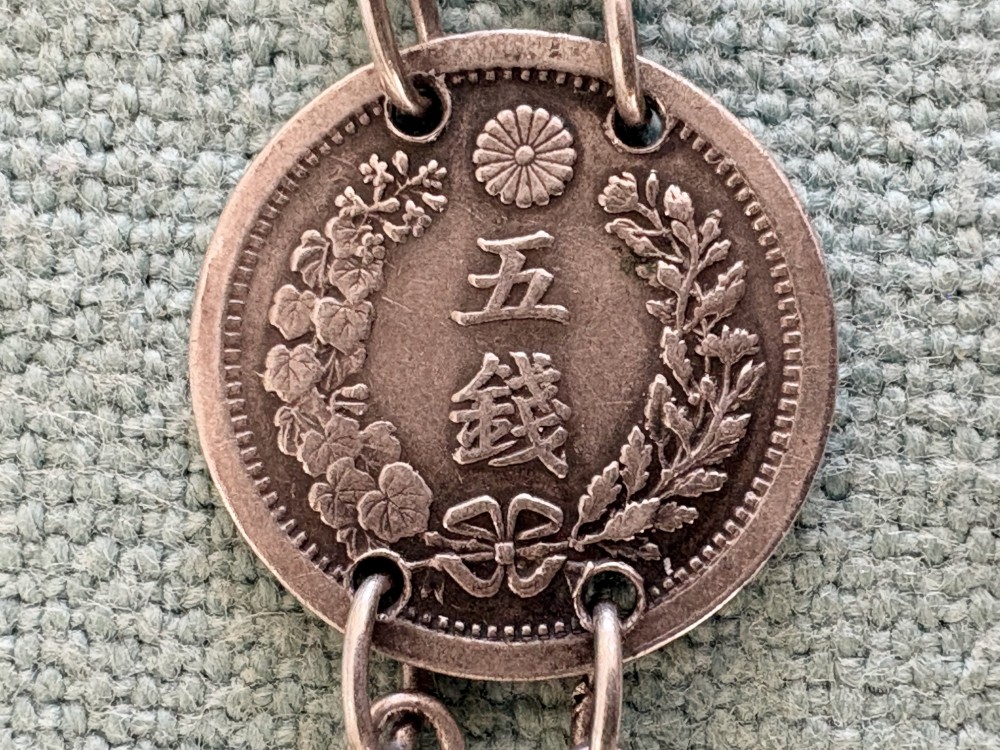 An antique silver pair-cased pocket watch featuring a white enamel dial with black Roman numerals, connected to a silver chain formed of linked coins, a T-bar, and a small cross charm. View VI
