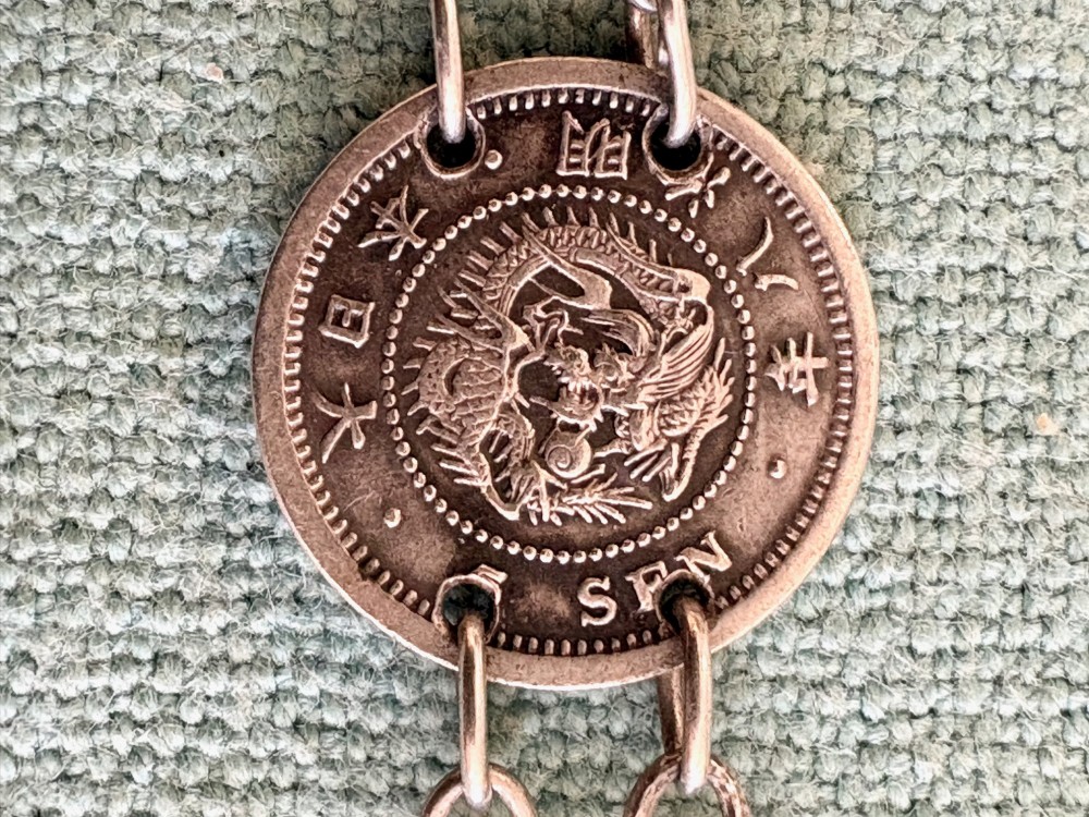 An antique silver pair-cased pocket watch featuring a white enamel dial with black Roman numerals, connected to a silver chain formed of linked coins, a T-bar, and a small cross charm. View VII