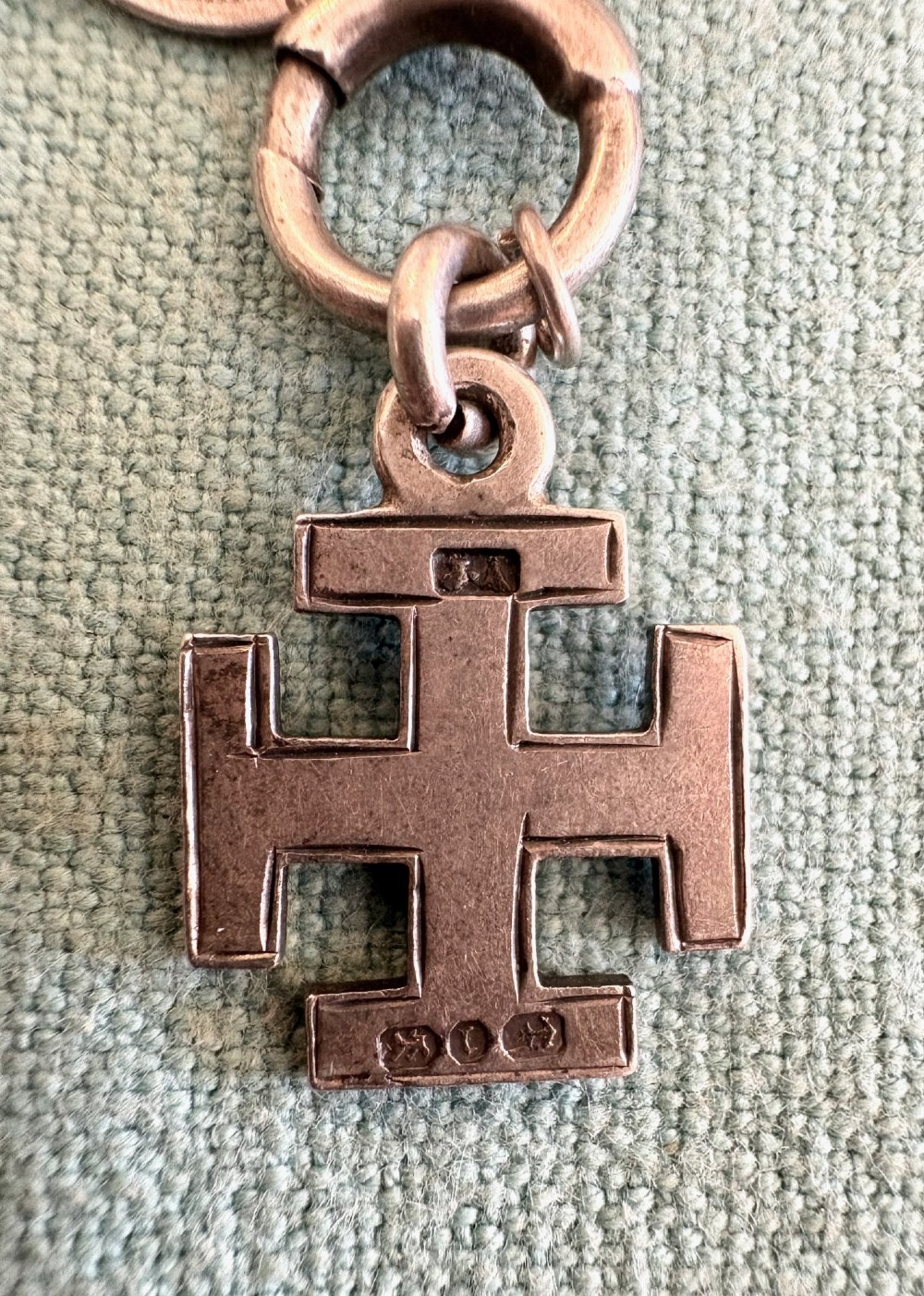 An antique silver pair-cased pocket watch featuring a white enamel dial with black Roman numerals, connected to a silver chain formed of linked coins, a T-bar, and a small cross charm. View VIII