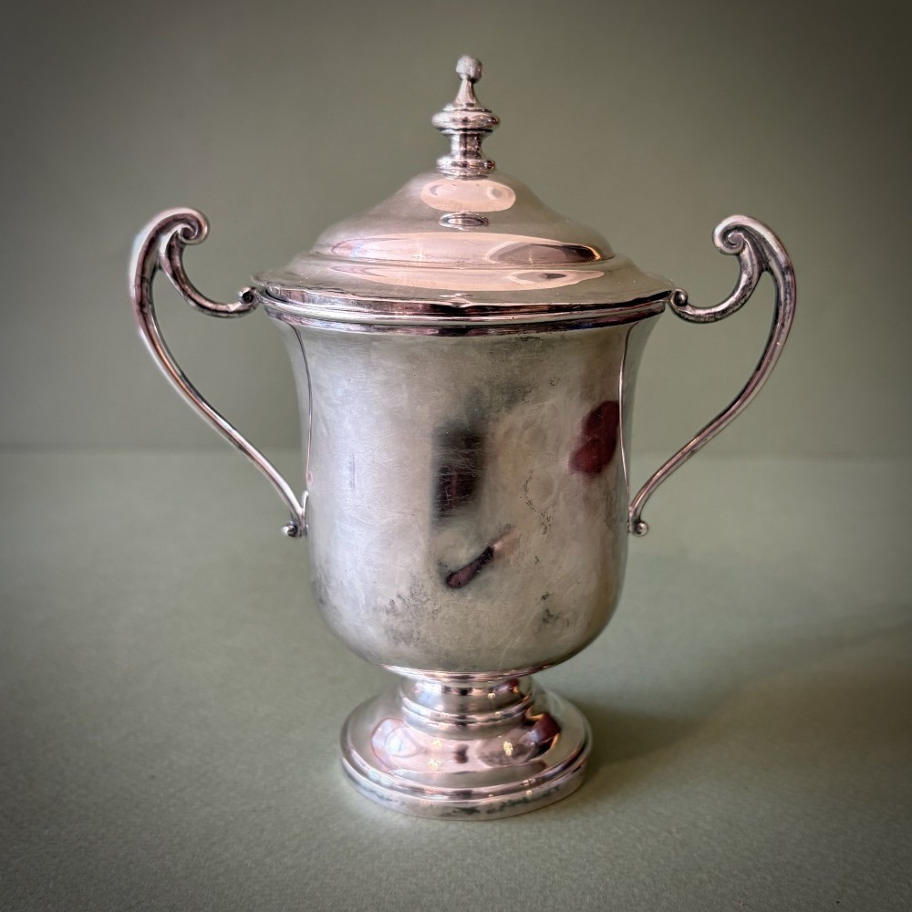 An antique silver two-handled cup featuring a fitted domed lid with a turned finial and a stepped pedestal foot.