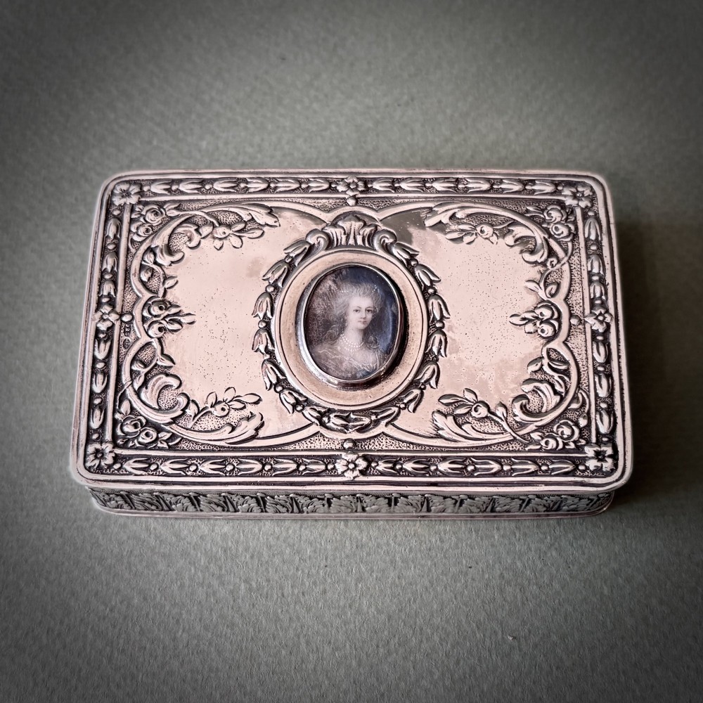 A rectangular silver snuff box decorated with floral relief work and a central oval portrait miniature of a woman. View VI
