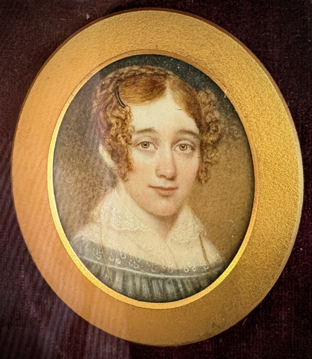 A pair of circular Regency-era miniature portraits set inside brass bezels mounted on plum velvet within a deep wooden frame. View II
