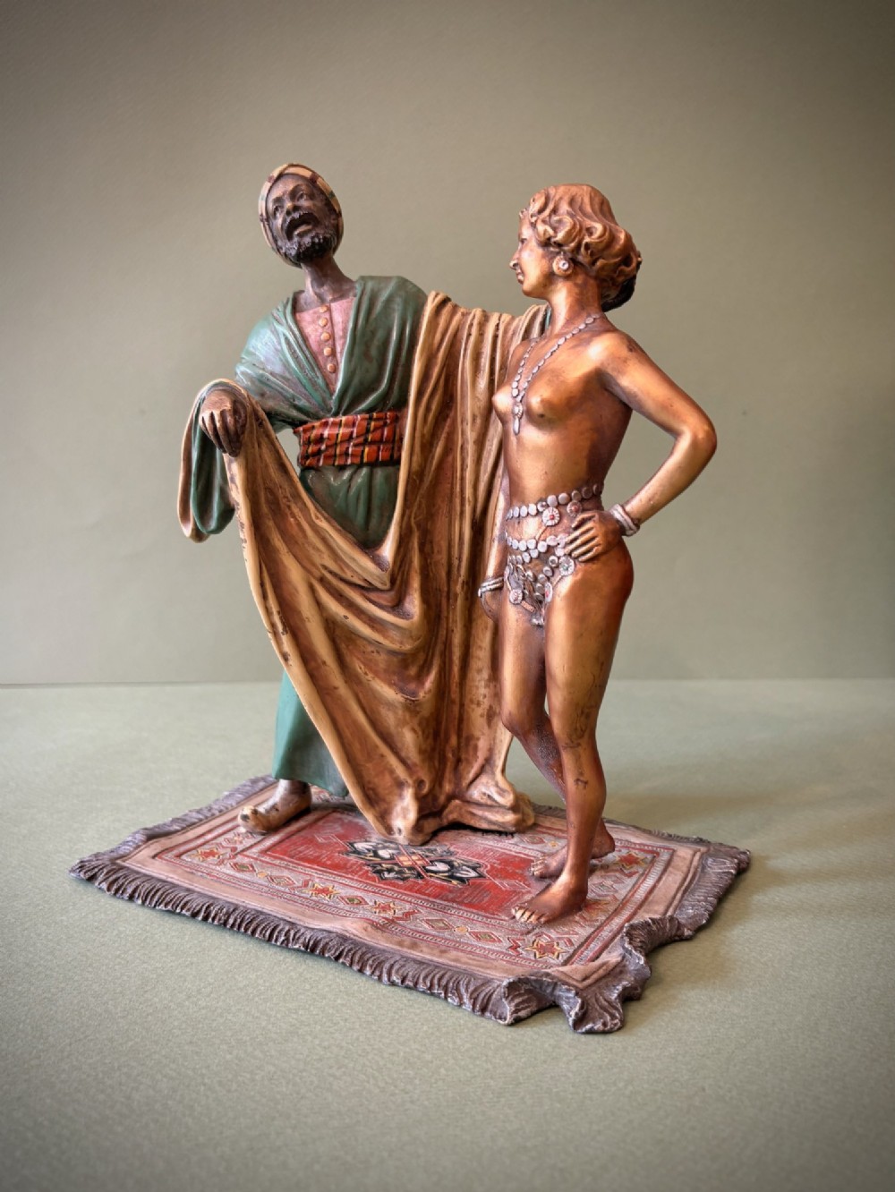 An Austrian cold-painted bronze figure group depicting a draped Orientalist figure standing beside a female figure on a patterned carpet base. View II