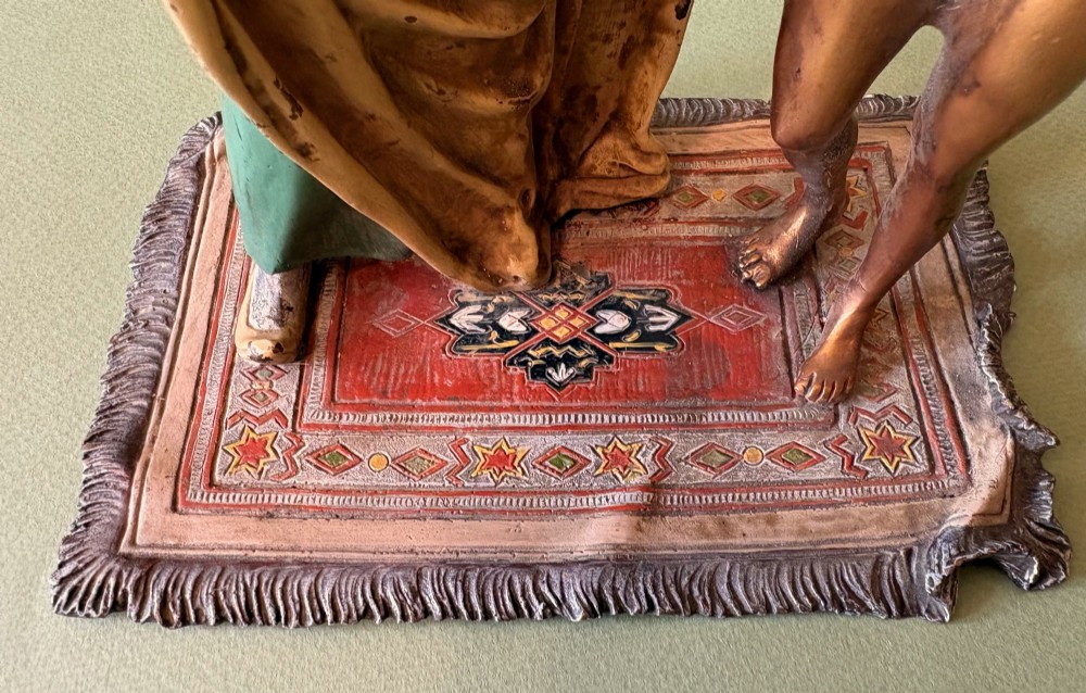 An Austrian cold-painted bronze figure group depicting a draped Orientalist figure standing beside a female figure on a patterned carpet base. View V