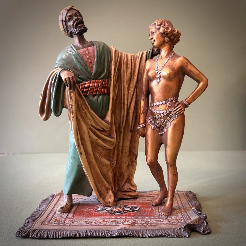 An Austrian cold-painted bronze figure group depicting a draped Orientalist figure standing beside a female figure on a patterned carpet base. View VII
