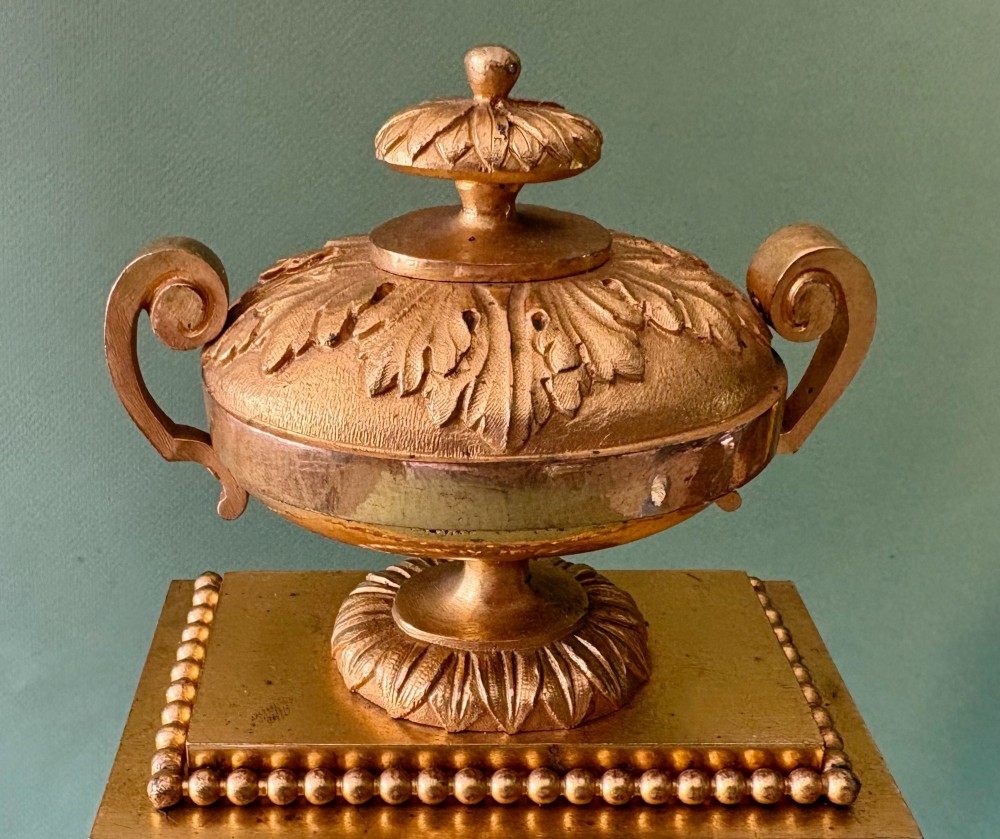 A 19th-century French gilt metal mantel clock featuring hand-painted green porcelain panels and an urn finial, displayed inside a glass dome on a wooden base. View V