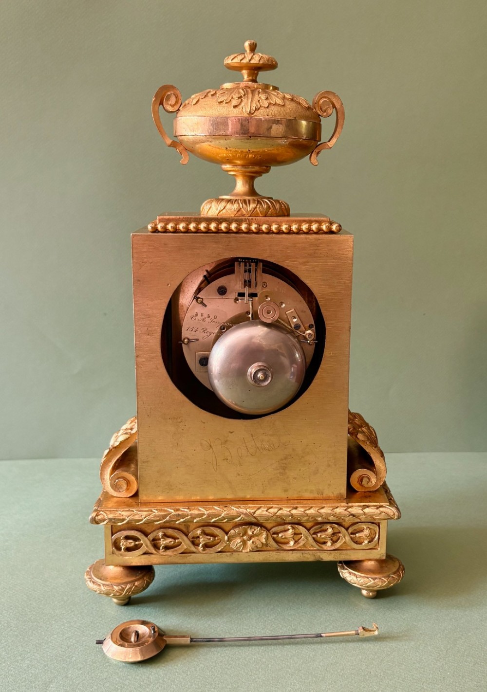 A 19th-century French gilt metal mantel clock featuring hand-painted green porcelain panels and an urn finial, displayed inside a glass dome on a wooden base. View VI