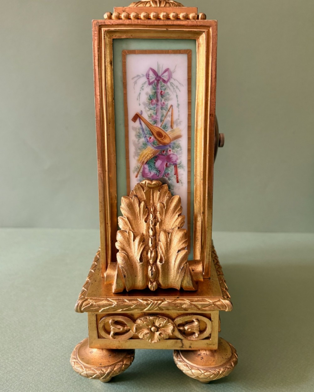 A 19th-century French gilt metal mantel clock featuring hand-painted green porcelain panels and an urn finial, displayed inside a glass dome on a wooden base. View VII