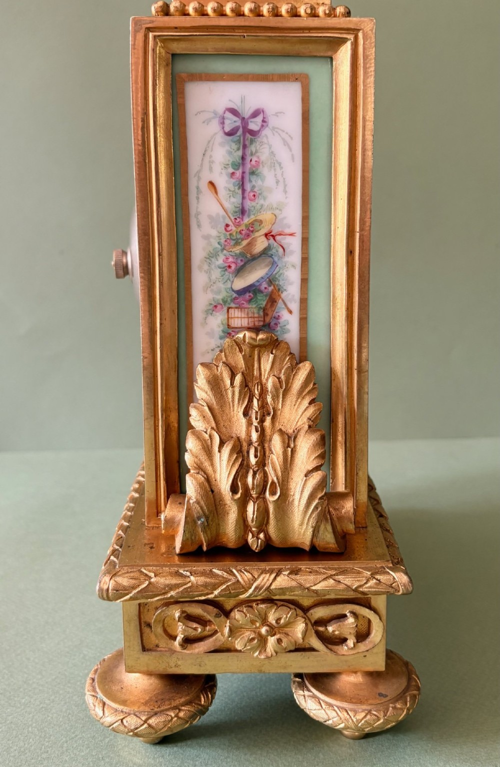 A 19th-century French gilt metal mantel clock featuring hand-painted green porcelain panels and an urn finial, displayed inside a glass dome on a wooden base. View VIII