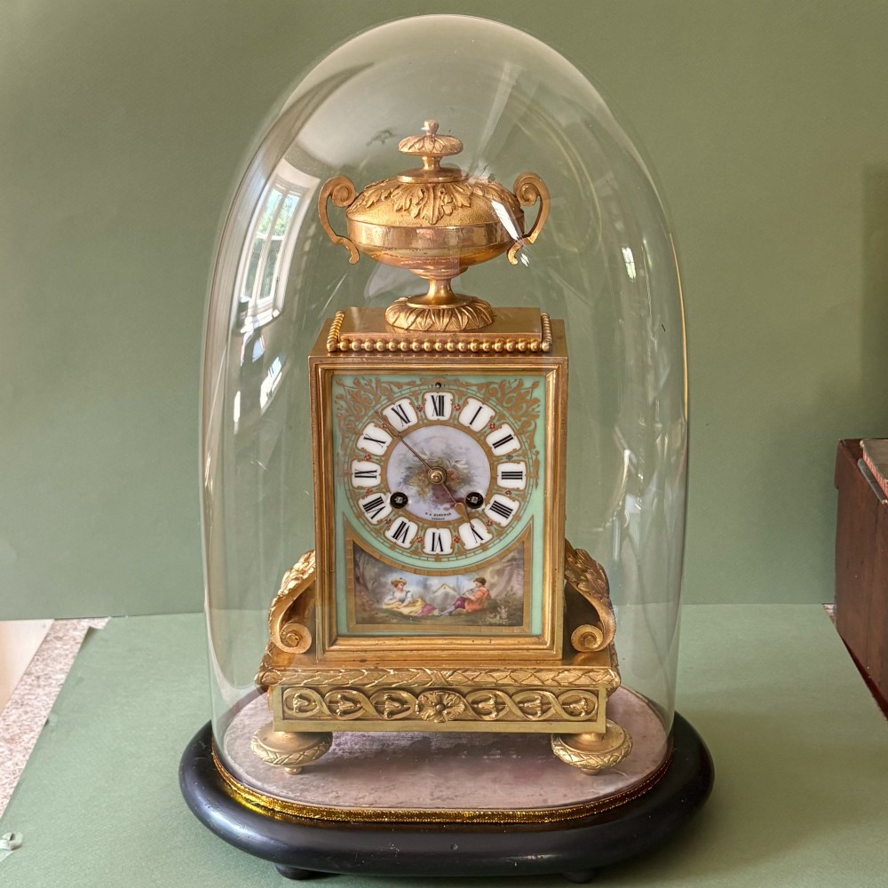 A 19th-century French gilt metal mantel clock featuring hand-painted green porcelain panels and an urn finial, displayed inside a glass dome on a wooden base. View IX