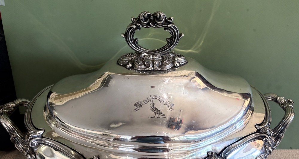 An antique silver-plated three-piece soup tureen featuring a domed lid with a scroll handle, engraved heraldic crest, and ornate scrolled feet. View II