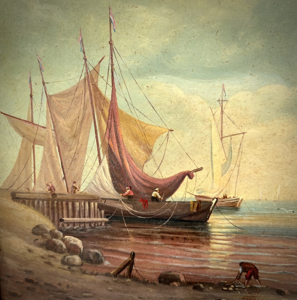 An antique oil painting on wood panel depicting sailing ships anchored along a sandy shore under a cloudy sky, held in an ornate gilt scrollwork frame. View IV