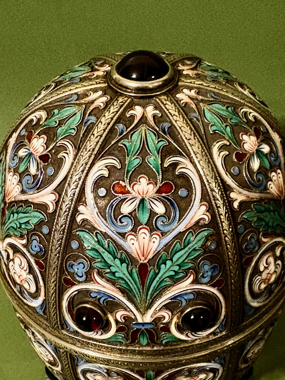 A Russian silver egg decorated with polychrome floral enamel scrolls and set with cabochon stones, resting on a tripod silver stand with hoofed feet. View III