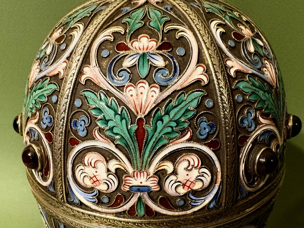 A Russian silver egg decorated with polychrome floral enamel scrolls and set with cabochon stones, resting on a tripod silver stand with hoofed feet. View VII
