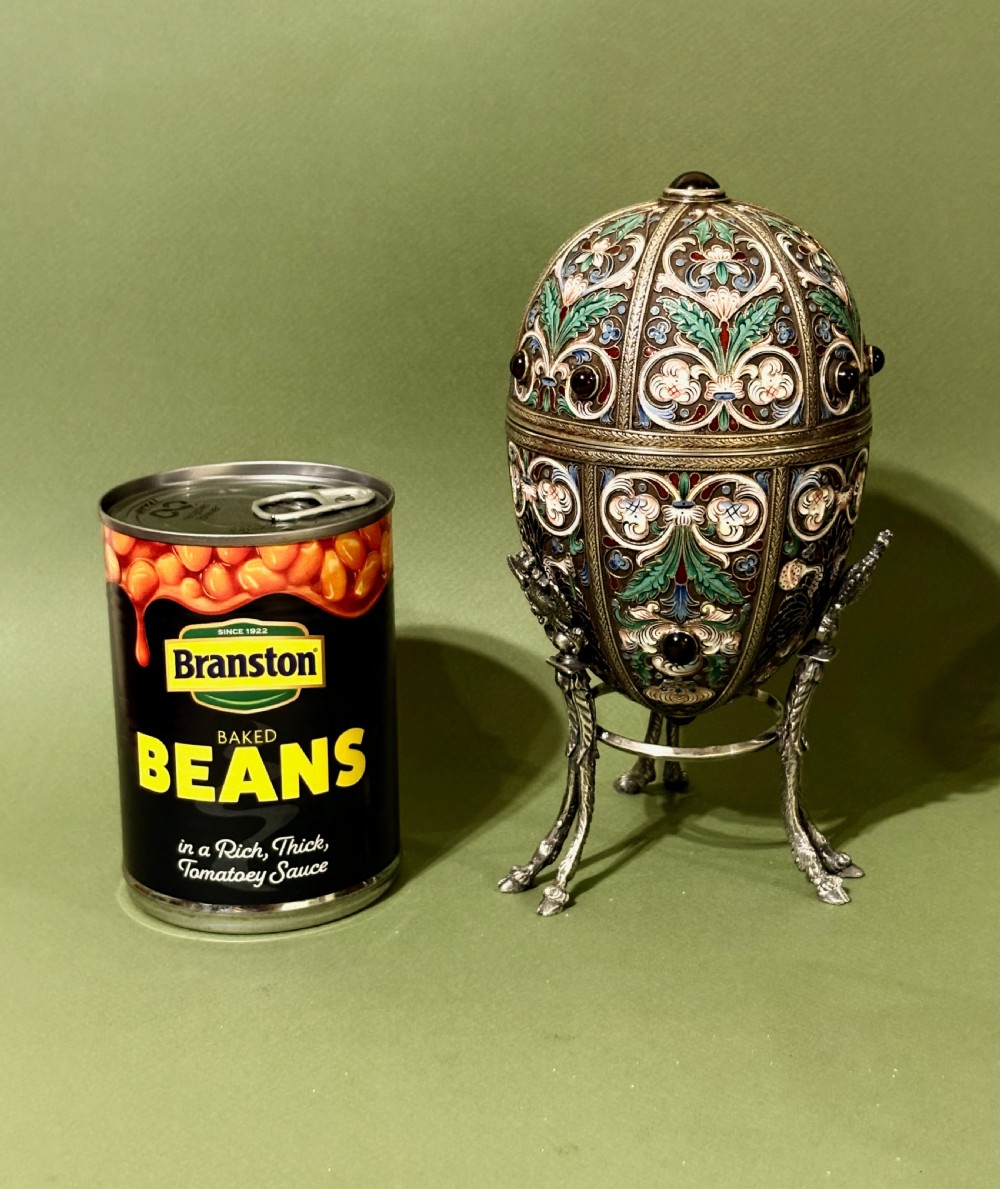 A Russian silver egg decorated with polychrome floral enamel scrolls and set with cabochon stones, resting on a tripod silver stand with hoofed feet. View XIII