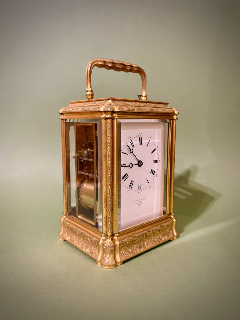 An antique rectangular French carriage clock featuring a gilt brass case with engraved foliage, glass side panels, a top carrying handle, and a white enamel dial displaying Roman numerals. View II